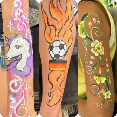 Drei bemalte Arme mit einem Einhorn, einem Feuerball mit Fußball und floralen Mustern.